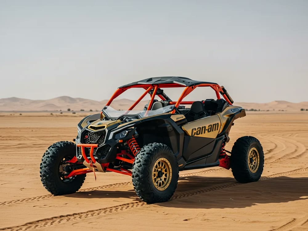 Gold and black Can-Am Maverick X3 dune buggy parked on flat Dubai desert sand